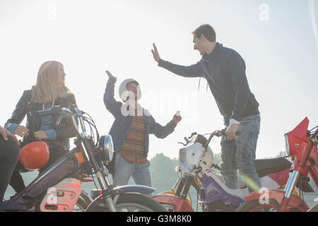 Groupe d'amis assis sur les cyclomoteurs, les deux hommes donnant cinq haut Banque D'Images