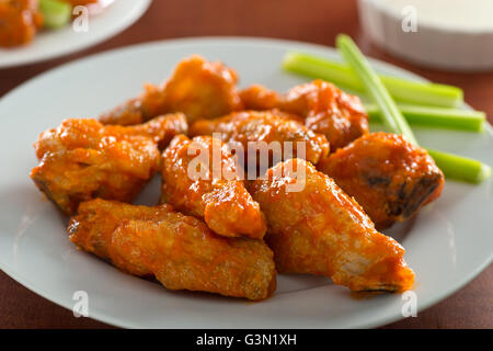 Une assiette de délicieuses ailes de poulet chaud épicé avec sauce sriracha et bâtonnets de céleri. Banque D'Images