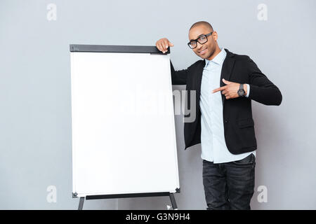 L'Afrique de l'heureux jeune homme à lunettes et permanent sur un tableau de pointage vierge Banque D'Images