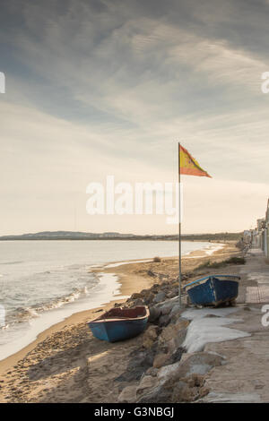 Deux petits bateaux sur une étroite plage de sable avec un drapeau espagne soufflant légèrement. Banque D'Images