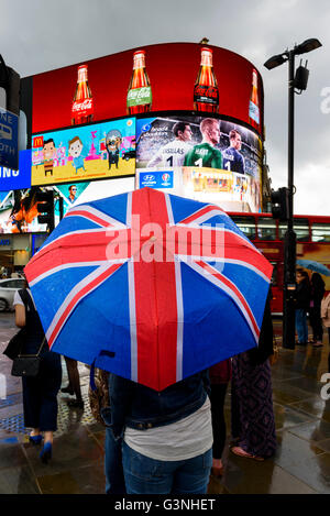 Les touristes avec Union Jack à Piccadilly Circus, parapluie un jour de pluie à Londres, au Royaume-Uni. Banque D'Images