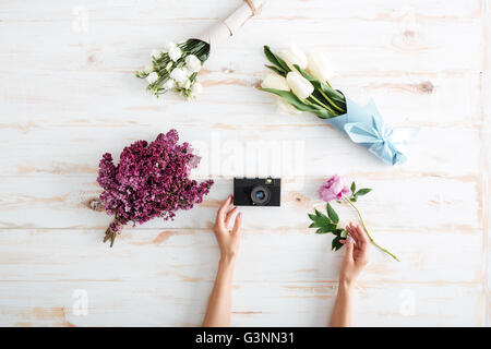 Mains de jeune femme mettre l'appareil photo et de bouquets de fleurs sur table en bois Banque D'Images