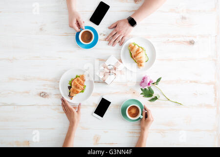 Les mains de l'homme et de la femme de boire du café avec les croissants sur table en bois avec les smartphones, l'écran vide et cadeau fleur Banque D'Images