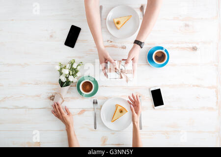 Mains de jeune homme à femme actuelle donnant sur table en bois avec des gâteaux, du café, des fleurs et les smartphones Banque D'Images