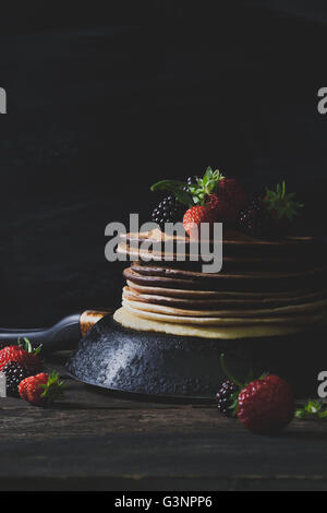 Crêpes au chocolat dans la casserole rouillée avec les fruits comme les fraises et les mûres sur la vieille table en bois, vertical Banque D'Images