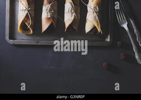 Crêpes de mûres sur rusty tinwere avec couteau et fourchette en argent sur tableau noir rayé, vue du dessus Banque D'Images