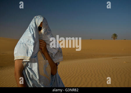 Un homme se tient sur une dune de sable avec le bleu et or tissu enroulé autour de sa tête et le visage pour le protéger de souffler à s Banque D'Images