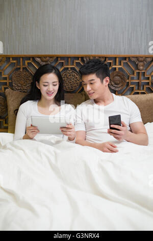 Happy young couple smart phone in bed Banque D'Images