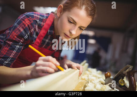 Female carpenter marquage sur planche en bois avec un crayon Banque D'Images