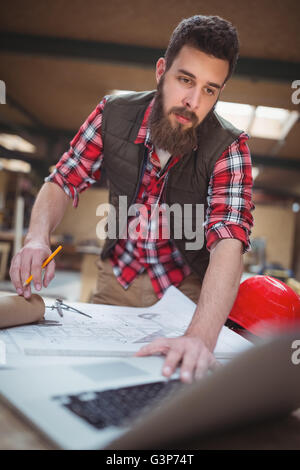 Carpenter using laptop tout en travaillant sur un plan Banque D'Images