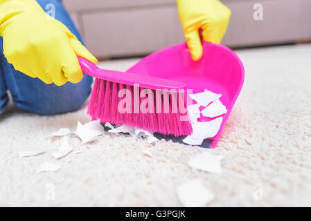 Les mains dans les gants jaune balayant un tapis brosse. Banque D'Images