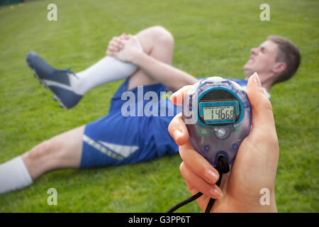 Image composite d'une main tenant une minuterie contre football player en bleu se trouvant blessé Banque D'Images