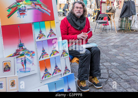 Artiste à Montmartre, Paris, assis à son chevalet avec son art finie. Ses peintures sont de la Tour Eiffel en différentes couleurs. Banque D'Images