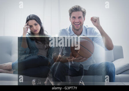 Image composite de l'homme qui regarde le sport à la télévision à côté de son épouse s'ennuie Banque D'Images