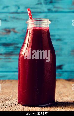 Libre d'un smoothie detox rouge servi dans une bouteille en verre avec une paille rouge à motifs de points blancs, sur un sol en bois rustique Banque D'Images