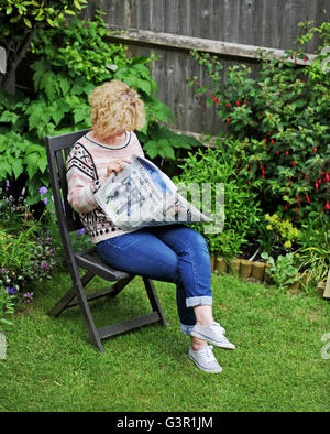 Femme lisant un journal dans le jardin en été UK Banque D'Images