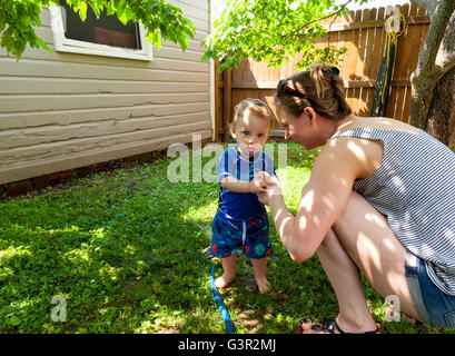 Bébé Caucasien Enfant et mère de jouer dans sa cour avec un jardin réseau sprinkleur Banque D'Images