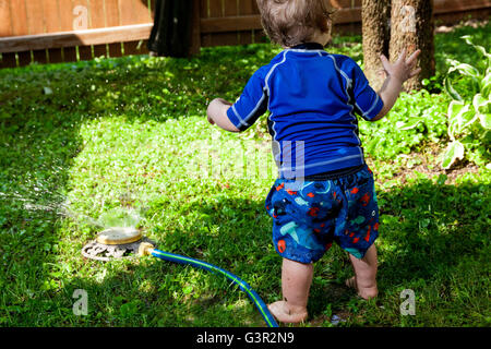 Bébé Caucasien Enfant et mère de jouer dans sa cour avec un jardin réseau sprinkleur Banque D'Images