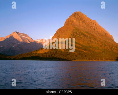 USA, Montana, le parc national des Glaciers, le lever du soleil la lumière sur Grinnell Point et plus lointain Mount Gould au-dessus du lac Swiftcurrent venteux. Banque D'Images