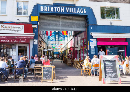 Les personnes mangeant à l'extérieur de l'entrée principale du village de Brixton Market, un marché communautaire multiculturel avec des boutiques indépendantes Banque D'Images