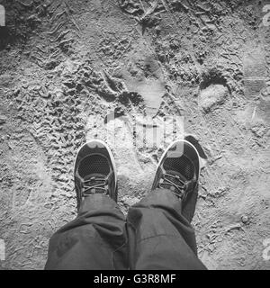 Pieds en chaussures hommes sportive sur route poussiéreuse, sale vue première personne, carré noir et blanc Banque D'Images