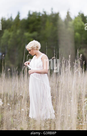 La Suède, Vastmanland, Teenage girl (16-17) in white dress standing in meadow parmi les plantes séchées