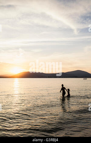 Italie, Sardaigne, Alghero, la mère et la fille de patauger dans la mer au coucher du soleil