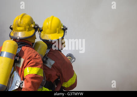 2 pompiers pulvériser de l'eau dans la lutte contre l'incendie avec le feu et la fumée sombre contexte Banque D'Images