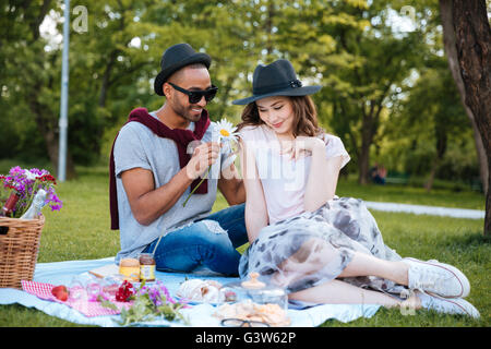 Smiling young man giving une fleur à sa copine on picnic in park Banque D'Images