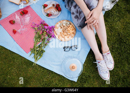 Belles jambes de jeune femme en blanc sneakers assis sur une couverture sur l'herbe verte et having picnic Banque D'Images