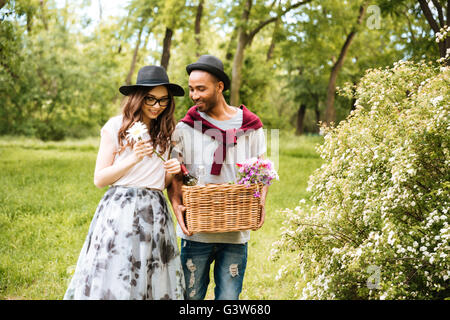 Happy young couple avec panier de boissons, de nourriture et de fleurs auront picninc in park Banque D'Images