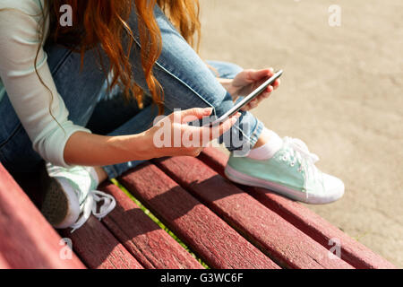 Jeune femme avec une tablette noir assis sur un banc dans un parc. Close up shot of hands holding tablet noir Banque D'Images