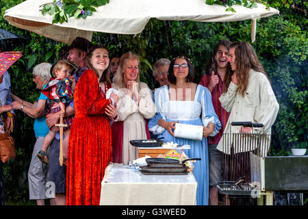 La population locale en costume médiéval à l'abri de la pluie sous un parapluie lors de la Foire Médiévale de Abinger, Surrey, UK Banque D'Images