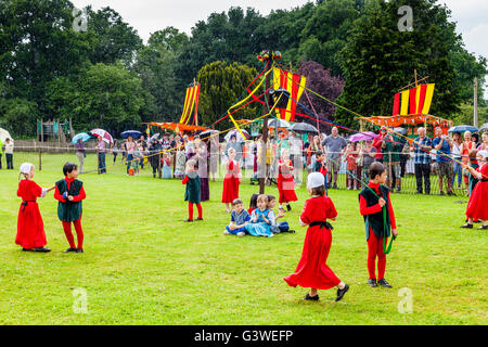 Les enfants en costume médiéval Maypole de danser dans la pluie pendant la Foire Médiévale à Abinger, Surrey, UK Banque D'Images