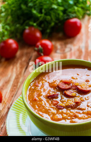 Soupe : soupe de tomate avec saucisse fumée, tomates et lentilles. Bol vert sur la table en bois. Les petites tomates cerises et laitue verte Banque D'Images