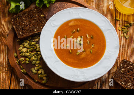 Soupe de carottes et de potiron avec les graines dans une assiette blanche sur le fond de bois. La laitue verte et d'huile d'olive. Banque D'Images