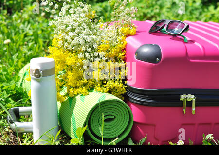 Valise rose avec thermos, fleurs sauvages et des tapis de yoga Banque D'Images