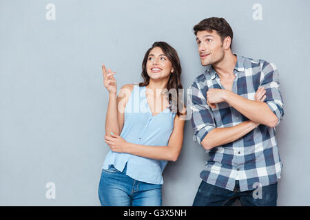 Attractive smiling couple standing et du doigt quelque chose sur fond blanc Banque D'Images