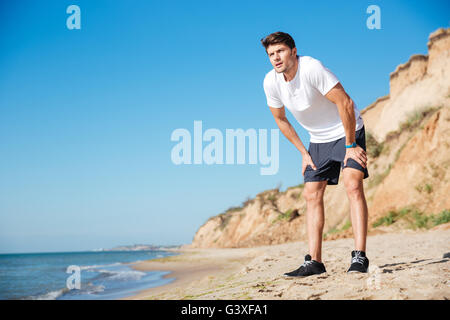 Beau assez jeune sportsman debout sur la plage Banque D'Images