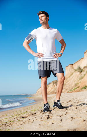Toute la longueur de l'attractive young sportsman avec cell phone debout sur la plage Banque D'Images