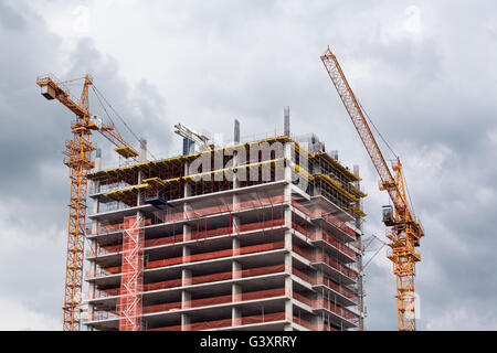 Site de construction avec des grues à tour contre ciel nuageux Banque D'Images