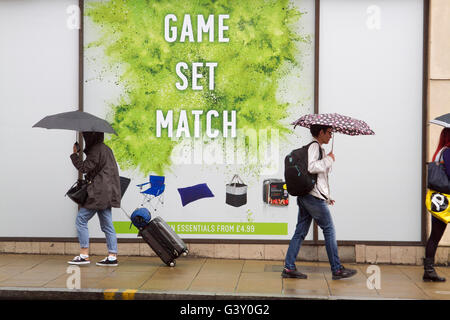 Wimbledon Londres, Royaume-Uni. 16 Juin, 2016. Les piétons à l'abri dans les parapluies devant une grande affiche de tennis avec les mots 'Jeu Set et Match' comme Wimbledon se prépare à accueillir les championnats de tennis Gazon 2016 Credit : amer ghazzal/Alamy Live News Banque D'Images