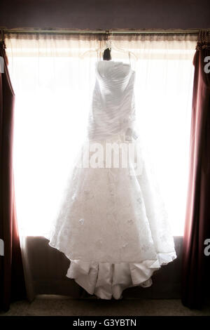 Une tête de satin robe de mariage est suspendu dans une suite nuptiale attendent la mariée à le mettre. Banque D'Images