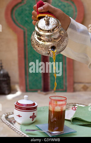 L'heure du thé à Marrakech, Maroc. Garçon verse le thé sucré au petit verre de la théière en argent Banque D'Images