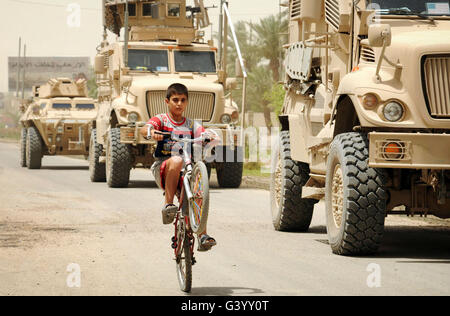 Un Irakien boy chevauche son vélo au-delà d'un véhicule militaire américain patrouille. Banque D'Images