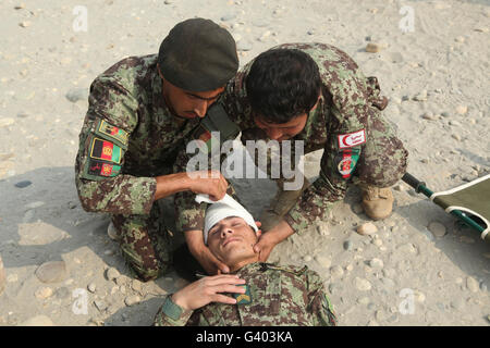 Les soldats de l'Armée nationale afghane mettre un bandage sur la tête d'un autre soldat. Banque D'Images