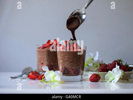 Dairy-free et chocolat végétalien et fraises du jour au lendemain de l'avoine dans les verres sur une surface blanche, chocolat fondu d'être arrosé sur Banque D'Images