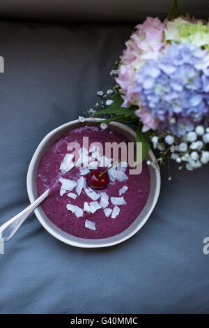 Cherry coconut smoothie dans un bol gris recouvert de flocons de noix de coco et un ensemble de Cherry Banque D'Images