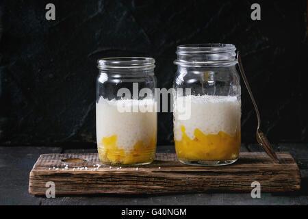 Des perles de tapioca au lait dessert avec du lait de coco et mangue. Servis dans des bocaux en verre sur vintage chopping board sur vieux bois Banque D'Images