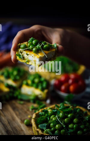 Main tenant une tranche de Tarte au fromage blanc garni de pois frais et d'herbes. Banque D'Images